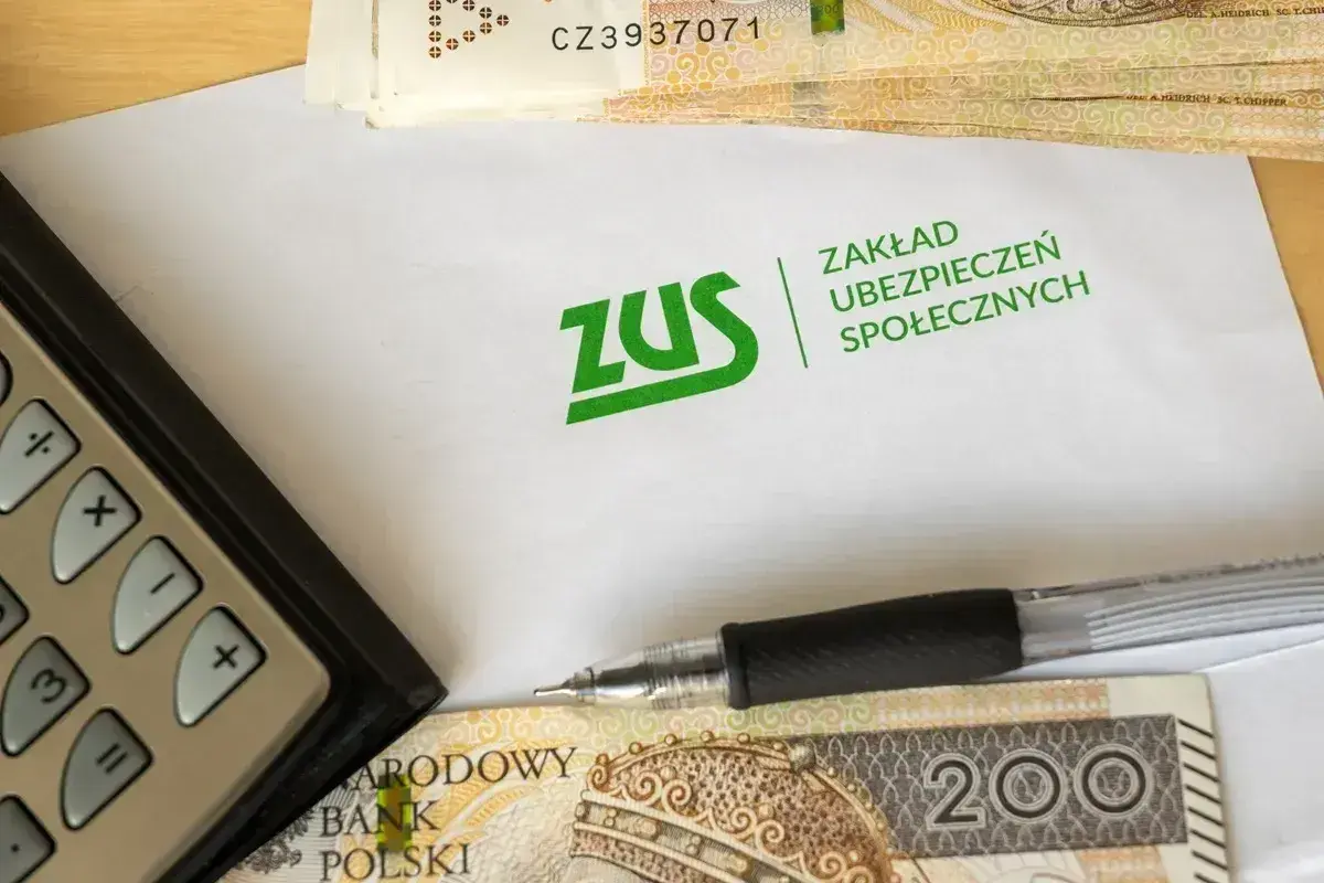 Kalkulator, długopis i pieniądze leżą obok koperty z logo ZUS. Temat: dziedziczenie składek ZUS.