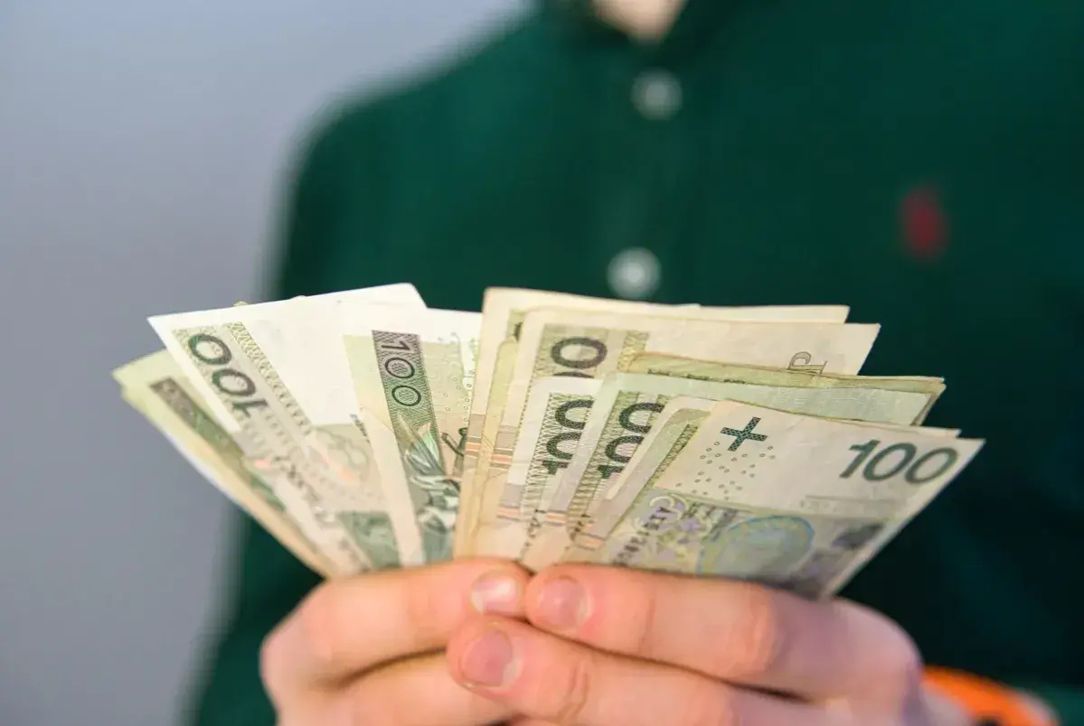 Dłonie trzymają plik banknotów 100 zł. To może być pomocne przy pytaniu, co to jest renta rodzinna.