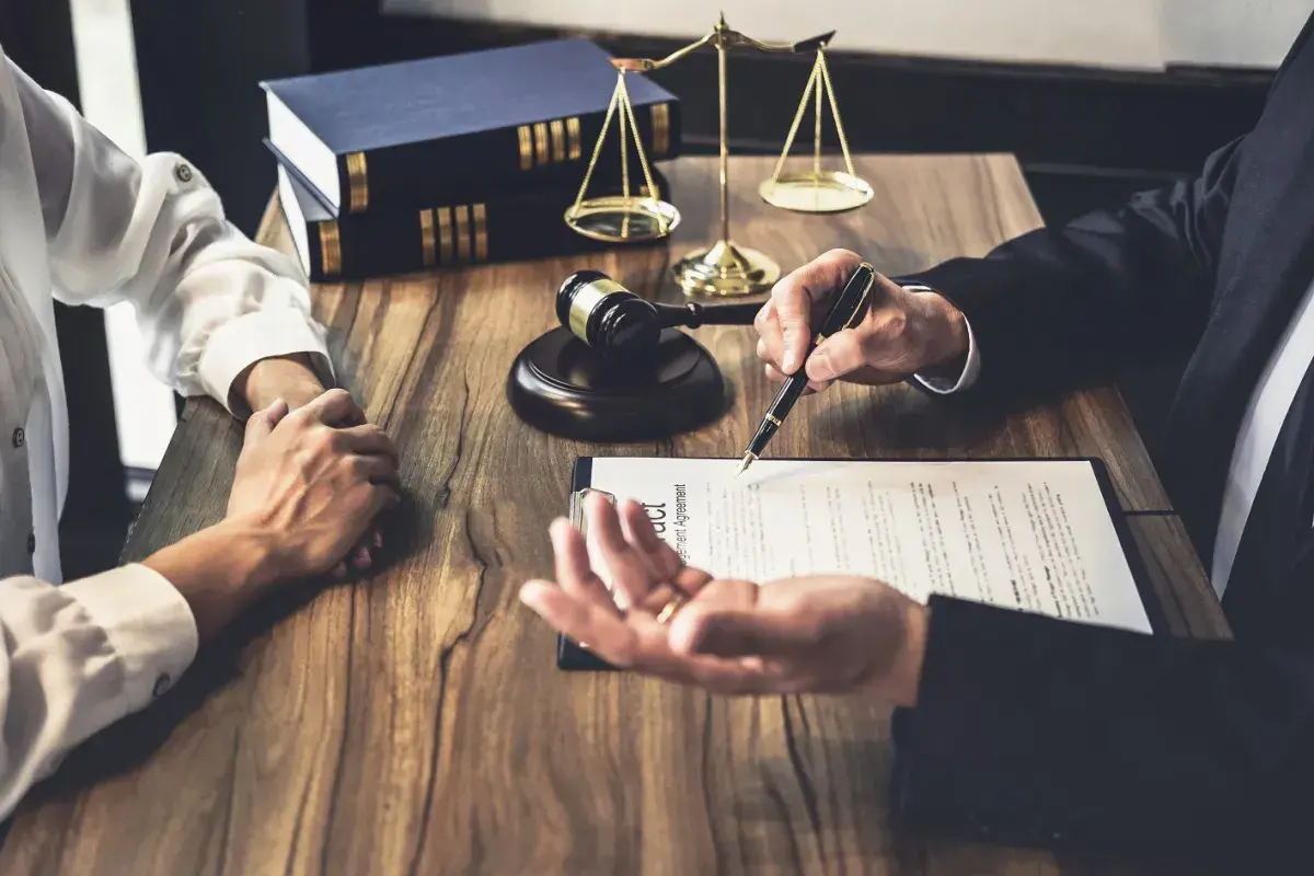 Prawnik omawia z klientem dokumenty, wskazując piórem na umowę. W tle waga sprawiedliwości i księgi. To ważny moment, by złożyć list intencyjny praca.