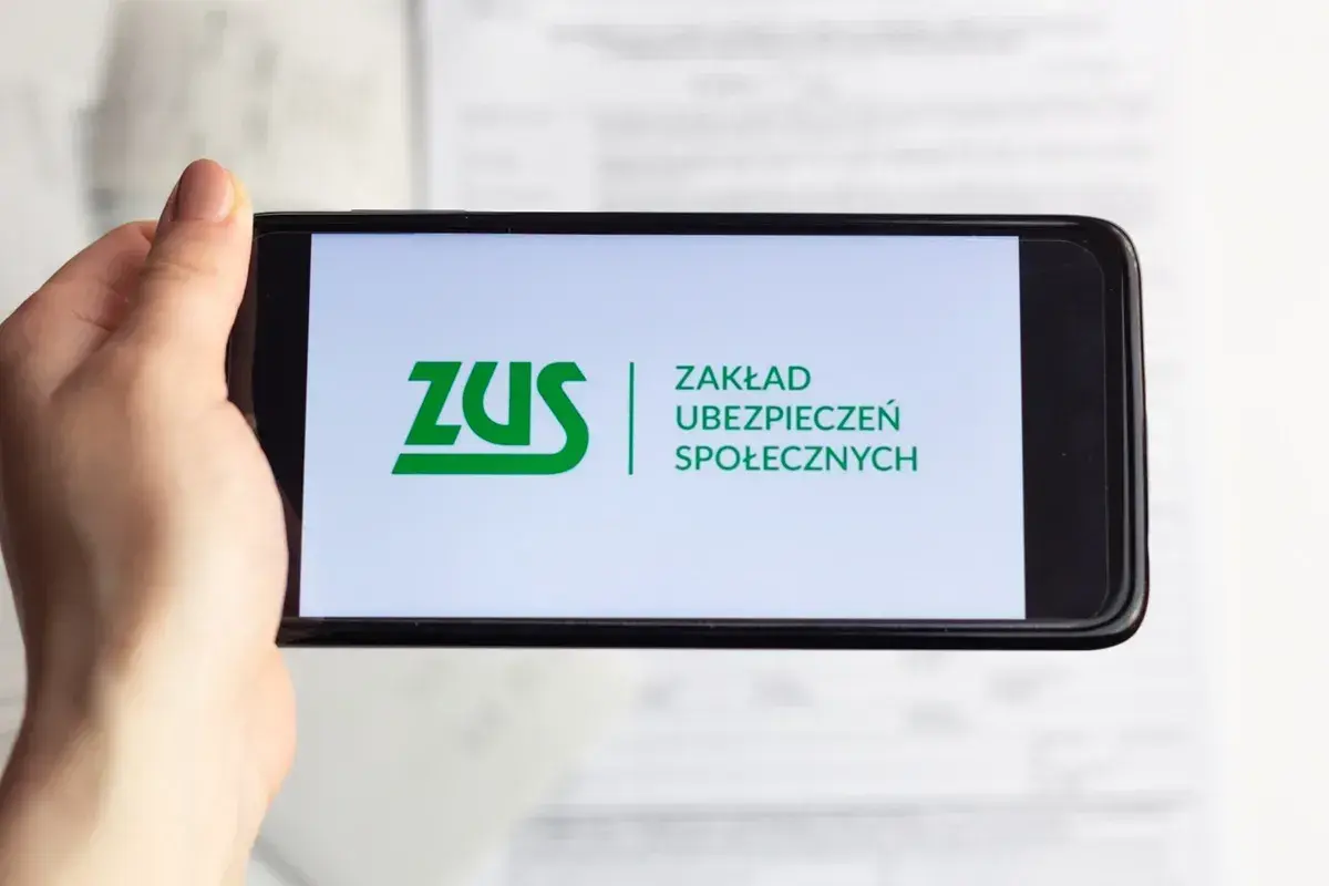Dłoń trzyma smartfon z logo ZUS. Możliwe, że sprawdzasz zwrot składki zdrowotnej.