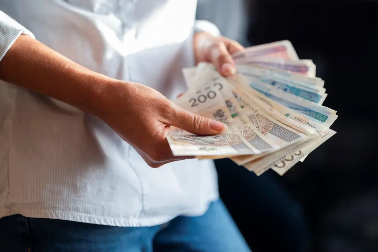 Dłonie trzymające plik banknotów. Wartość najniższej krajowej brutto jest tematem dyskusji, a pieniądze symbolizują zarobki.