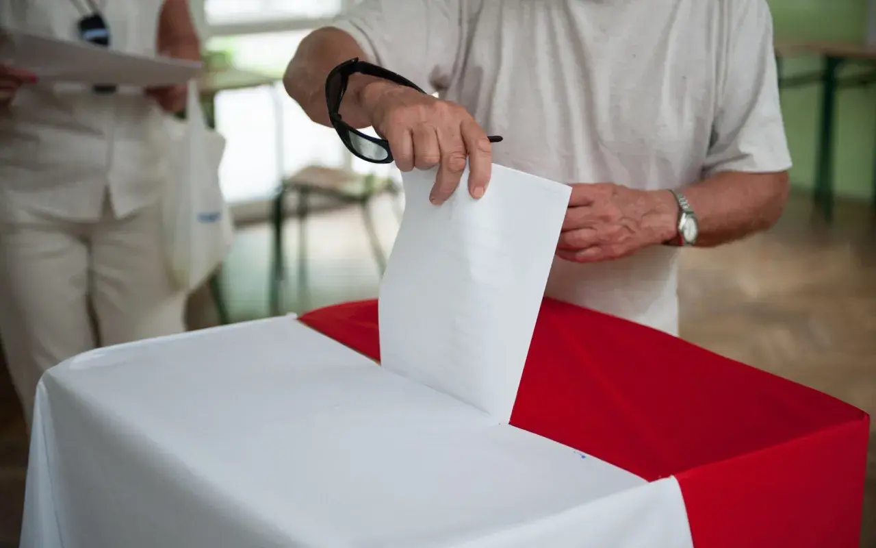 Mężczyzna wrzuca kartę do urny. Dowiedz się, jak głosować poza miejscem zamieszkania, aby Twój głos się liczył.