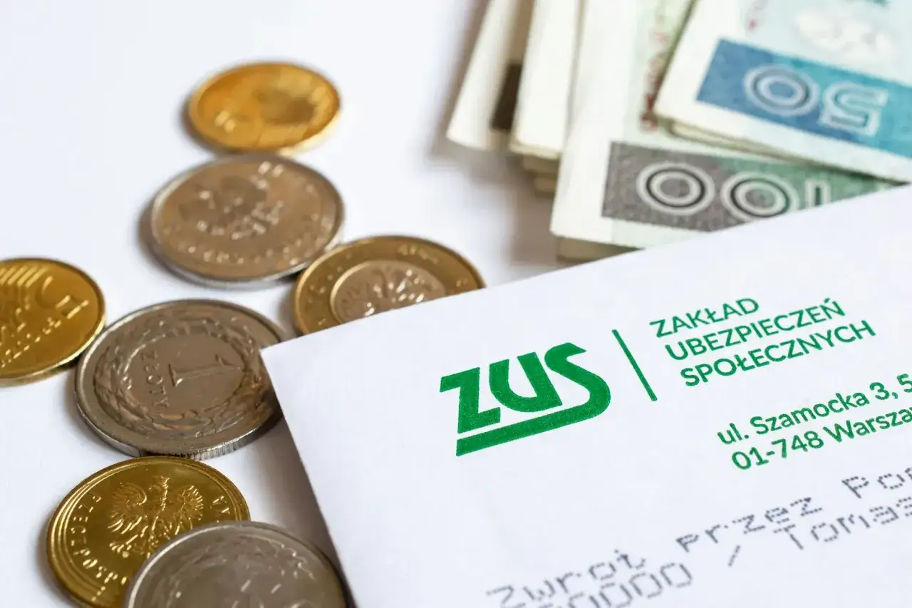 Monety i banknoty obok dokumentu ZUS, symbolizujące wypłatę gwarantowaną ZUS.