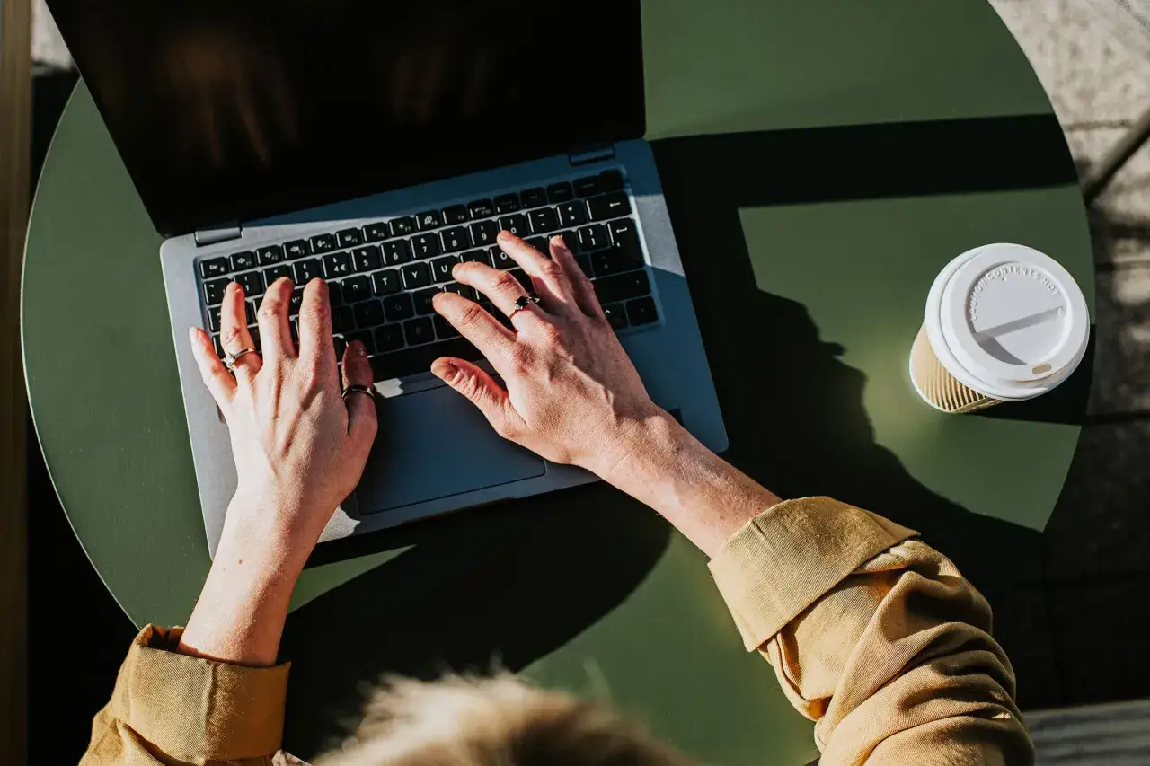 Kto to freelancer? Osoba pracująca zdalnie na laptopie, z kawą obok, w słoneczny dzień.