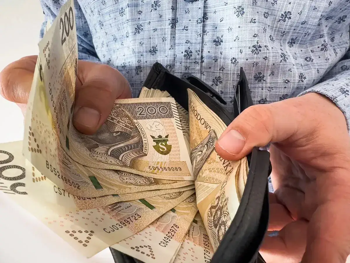 Ręce trzymają portfel z polskimi banknotami 200 zł. To może być nagroda za jubileusz w pracy.