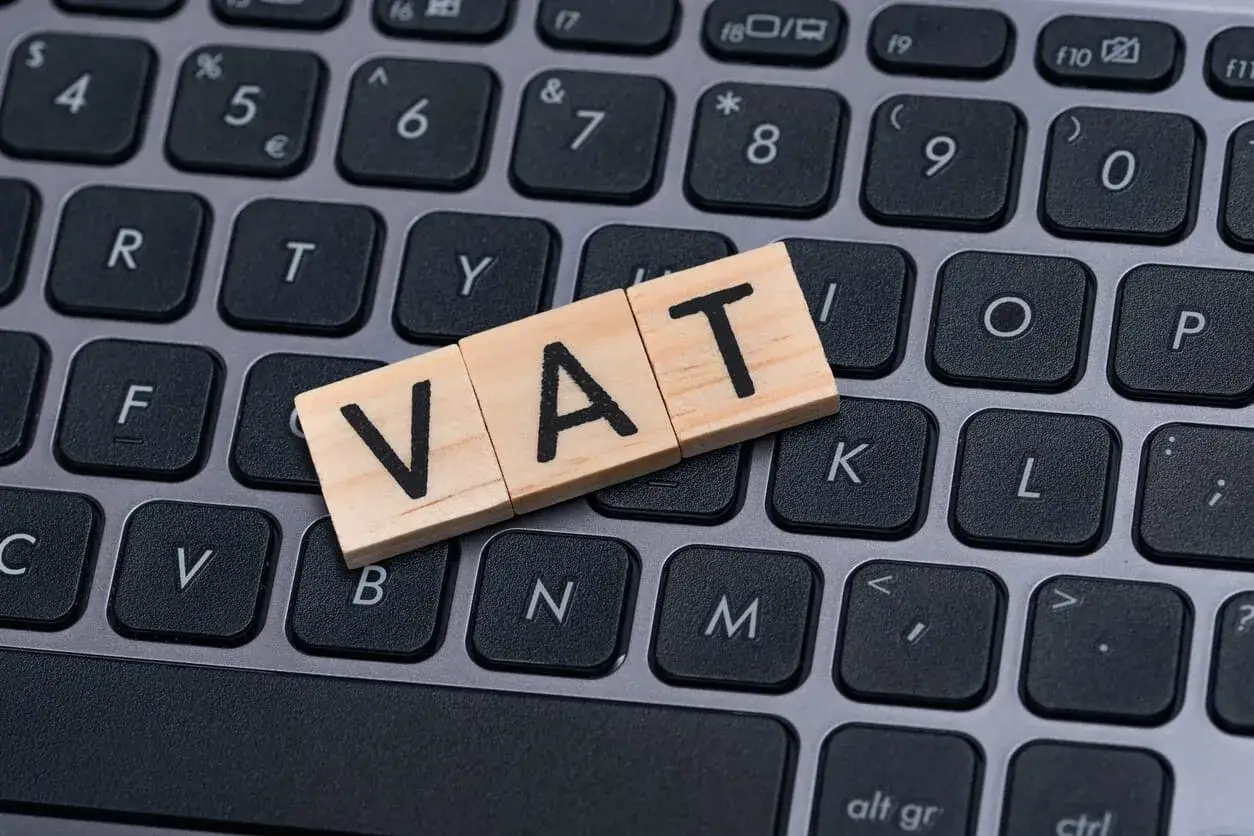 Drewniane klocki z literami VAT leżą na klawiaturze. Symbolizują przygotowanie wniosku o stwierdzenie nadpłaty VAT.