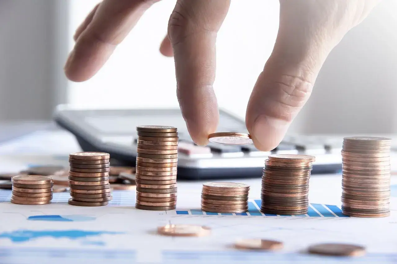 Dłoń układa monety na stosach, symbolizując rozw&oacute;j finansowy i faktoring dla firm.