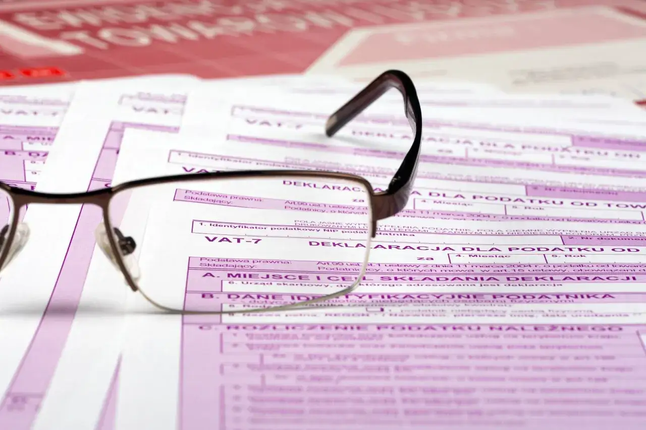Okulary leżą na deklaracjach VAT-7, symbolizując obowiązek podatkowy VAT.