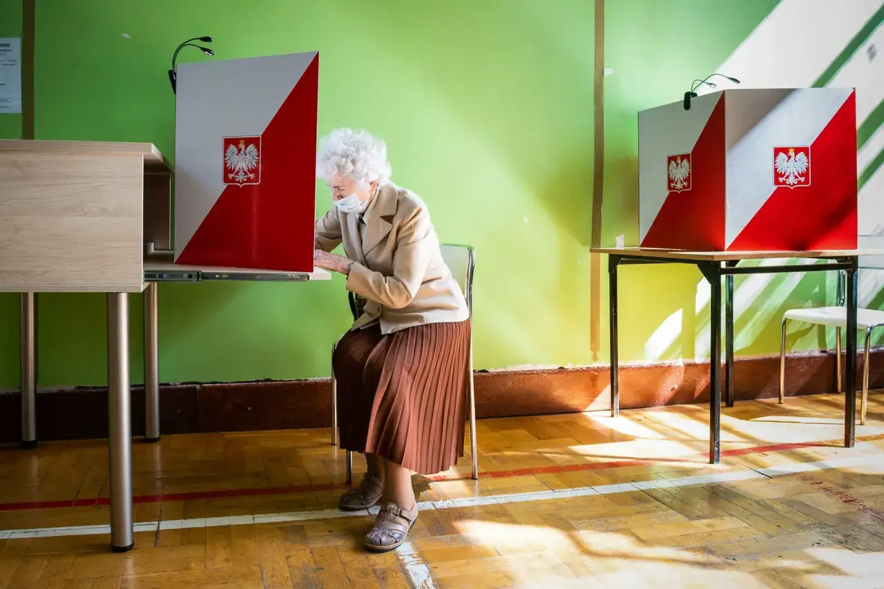 Starsza pani w maseczce głosuje w lokalu wyborczym. Dowiedz się, jak głosować poza miejscem zamieszkania.