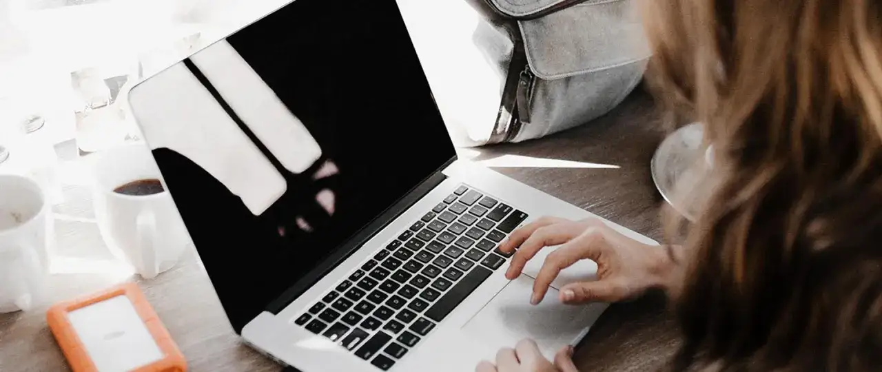 Kobieta szuka informacji, jak się zwolnić żeby dostać zasiłek dla bezrobotnych. Na biurku laptop, kawa i dysk zewnętrzny.