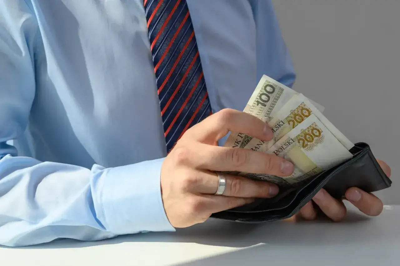 Mężczyzna w koszuli i krawacie wkłada polskie banknoty do portfela. To może być przykład, jak działa faktoring co to jest.
