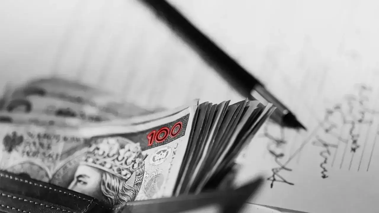 Stos banknotów 100 zł w portfelu, obok długopis i dokumenty. Czy to opóźnienie w płatnościach, czy celowa zwłoka?
