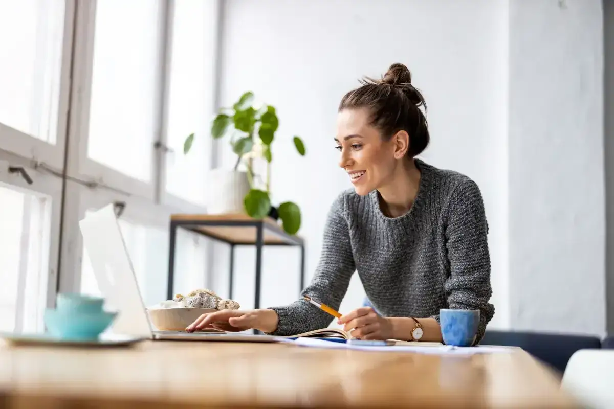 Uśmiechnięta kobieta pracuje przy laptopie, planując swoje 2 dni wolne za pracę w niedzielę.