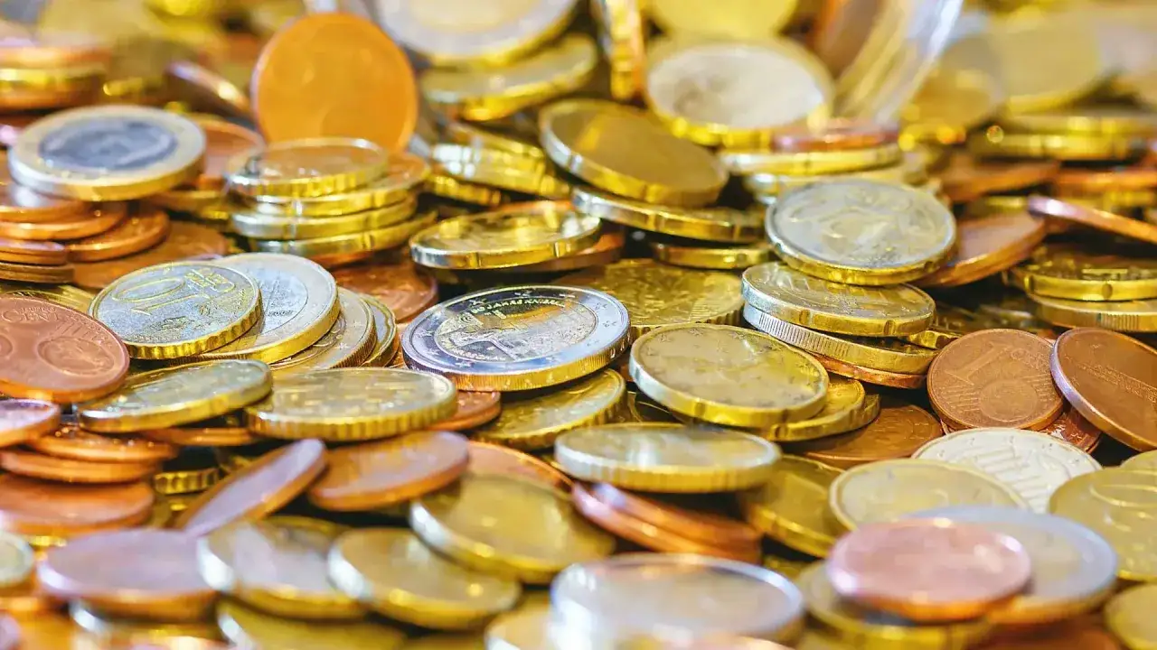G&oacute;ra monet euro, symbolizująca doch&oacute;d. Widać monety o r&oacute;żnych nominałach i kolorach, błyszczące w świetle.