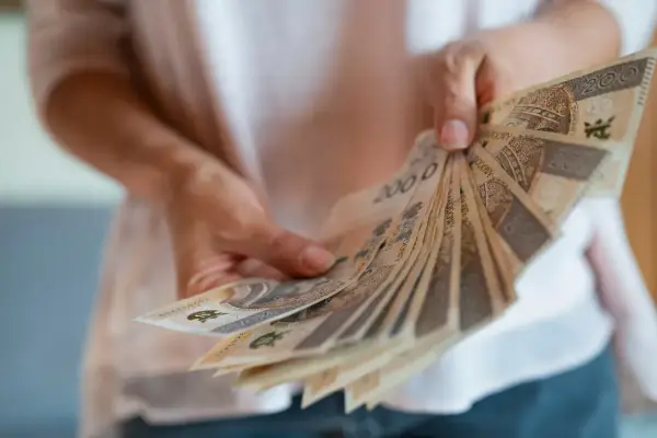 Dłonie trzymają wachlarz banknotów 200 zł. To nagroda za długoletni jubileusz w pracy.